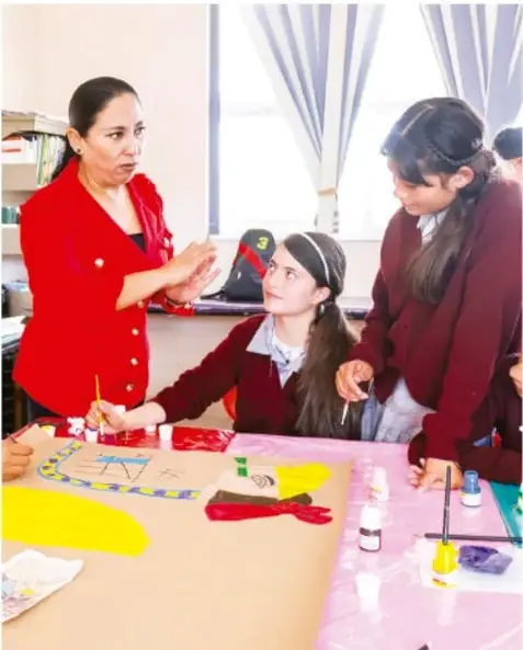 Fotografía de una docente con estudiantes trabajando con materiales de arte (papeles de colores, pinturas, tijeras) sobre una mesa, en la planeación de actividades del proyecto.