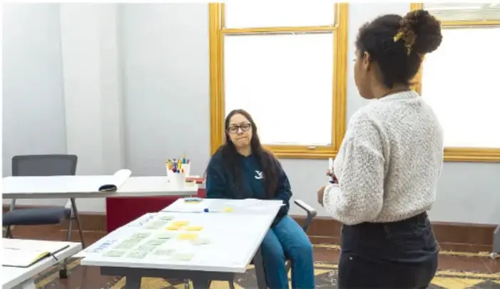 Fotografía de estudiantes trabajando en equipo alrededor de una mesa con fichas de colores, un organizador gráfico en cartulina y materiales de escritura.