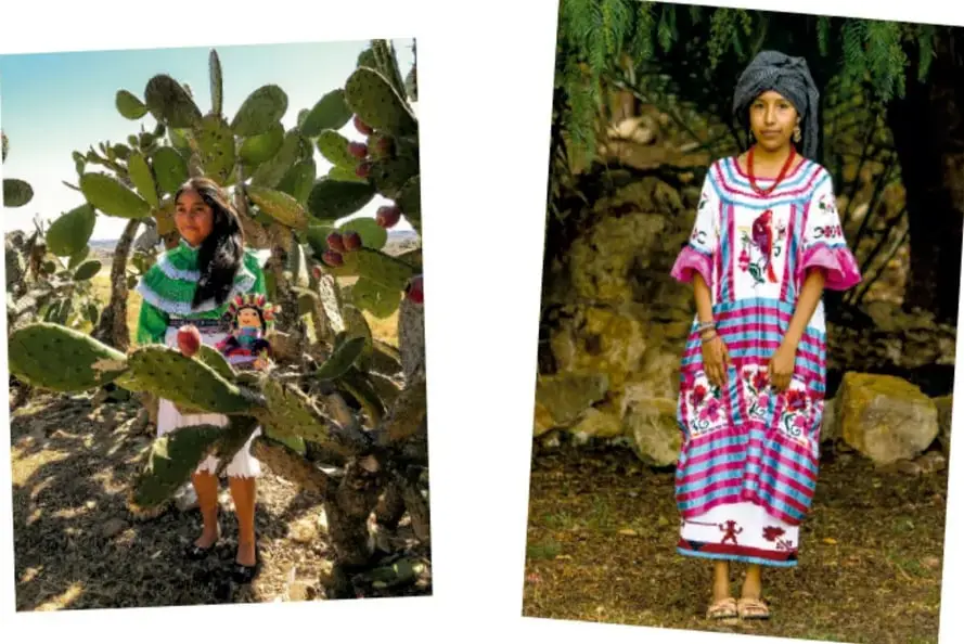 Niña con blusa verde y blanco de bordados, de pie junto a un nopal grande con tunas, en un paisaje árido.