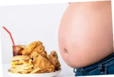 Fotografía de una persona con sobrepeso abdominal junto a una bandeja con comida rápida y un refresco, que ilustra la relación entre mala alimentación y obesidad.