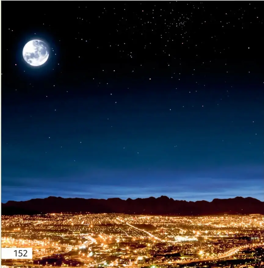 Fotografía nocturna de la Luna llena brillando en un cielo estrellado sobre el horizonte de una ciudad iluminada, con cerros al fondo.