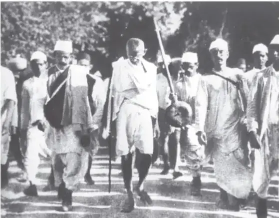 Retrato fotográfico de Mahatma Gandhi joven, con traje y corbata, brazos cruzados.