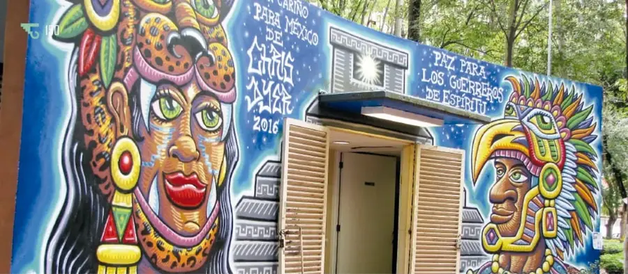 Mural colorido sobre la fachada de una caseta: mujer guerrera con penacho y jaguar, guerrero con penacho de plumas, pirámide y letreros como "Cariño para México de Chris Dyer 2016" y "Paz para los guerreros de espíritu".