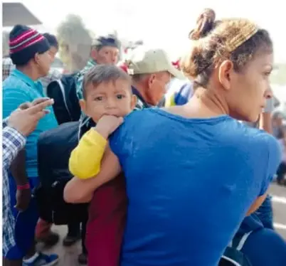 Mujer cargando a un niño en medio de una multitud, simbolizando la diversidad y el derecho a una vida digna.