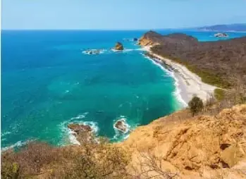 Fotografía costera del Parque Nacional Machalilla, con mar, playas, rocas y vegetación seca.