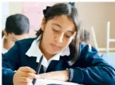 Fotografía de una estudiante de telesecundaria escribiendo en su cuaderno, concentrada, en el aula.