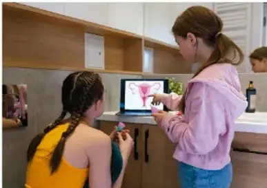 Dos adolescentes frente a una computadora, una de ellas señala la pantalla, en un ambiente de aprendizaje.