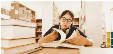 Fotografía de una joven leyendo un libro entre estanterías de una biblioteca.