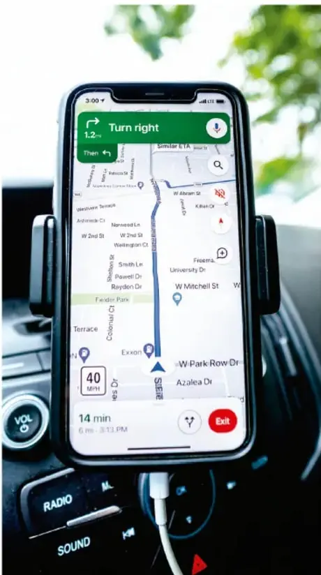 Teléfono inteligente colocado en un soporte dentro de un automóvil, mostrando una aplicación de navegación GPS con mapa, indicación 'Turn right', velocidad máxima 40 mph y tiempo estimado de llegada de 14 min; ilustra la función de navegar por internet con mapas.