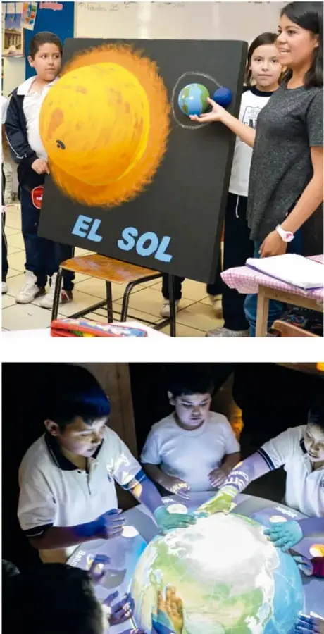 Niños y su maestra presentan un póster pintado de 'EL SOL' en un aula; la maestra sostiene un planeta pequeño.
