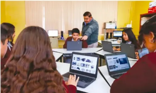 Fotografía de un grupo de estudiantes con laptops alrededor de una mesa, acompañados por su maestro, trabajando en el proyecto académico.
