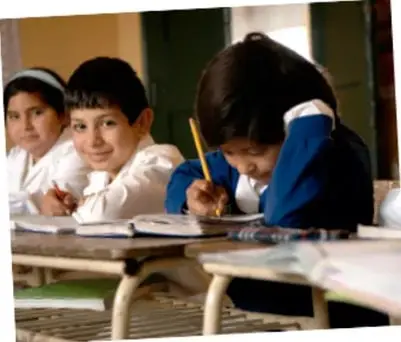 Fotografía de tres estudiantes de primaria sentados en un pupitre, escribiendo en sus cuadernos durante una actividad escolar.