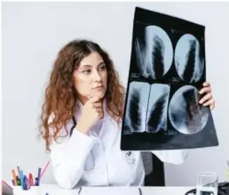 Fotografía de una profesional de la salud sosteniendo una radiografía de tórax frente a una fuente de luz.