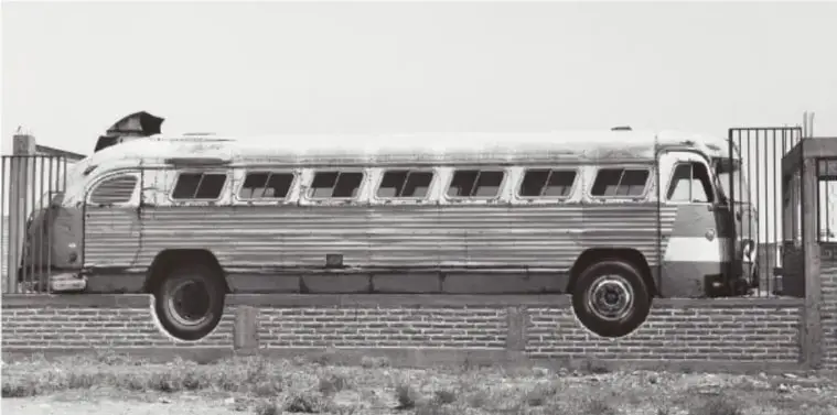 Fotografía en blanco y negro de un autobús antiguo montado sobre un muro de tabique, junto a una reja; Barda móvil, 1993, Santiaguillo, Zacatecas, de Mariana Yampolsky (1925-2002).