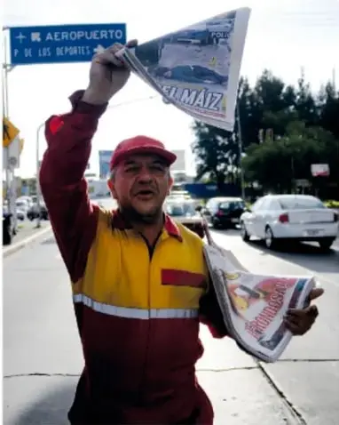 Vendedor de periódicos con gorra roja levanta un diario y un cartel que dice '¡EXTRA!' junto a un letrero de AEROPUERTO.