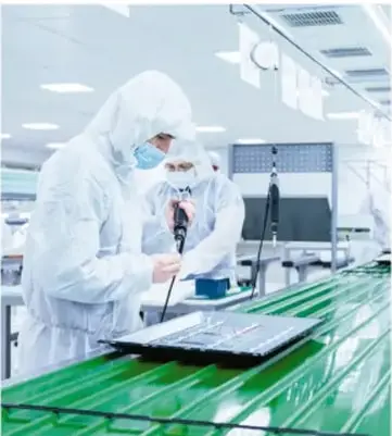 Persona con traje de protección blanco, mascarilla y gafas trabaja con una tableta sobre una superficie verde en un entorno industrial o agrícola.