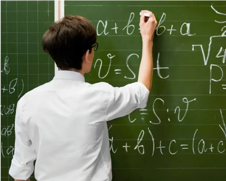 Fotografía de un estudiante de espaldas escribiendo con gis expresiones algebraicas en un pizarrón verde: a+b=b+a, v=S·t, t=S÷v, (a+b)+c=(a+c)+b y una raíz cuadrada.