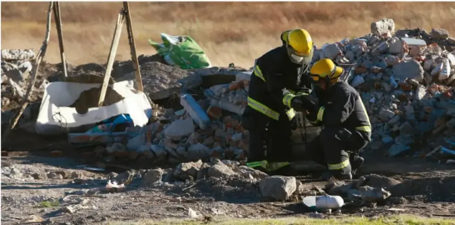 Dos rescatistas o bomberos con cascos amarillos y ropa de protección trabajan entre los escombros de un derrumbe o zona de destrucción, representando la labor de instituciones de apoyo ante desastres.