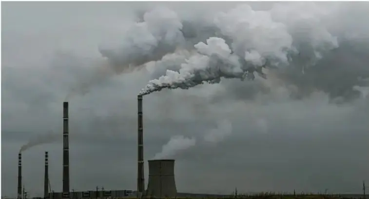 Fotografía de una planta industrial con chimeneas que emiten grandes columnas de humo gris hacia un cielo nublado, ilustrando las emisiones contaminantes como causa del cambio climático.