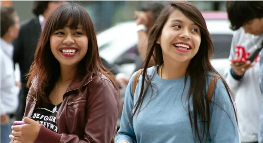 Fotografía de dos jóvenes sonriendo en la calle, ilustrando la interacción placentera con los demás y los hábitos activos y saludables.