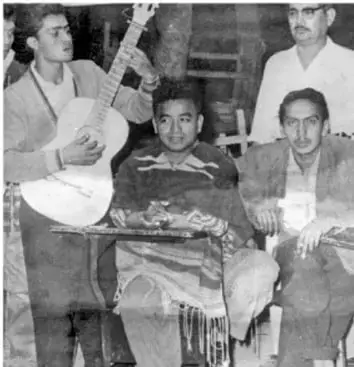 Fotografía en blanco y negro de un grupo de hombres, algunos con instrumentos musicales, en un espacio interior.