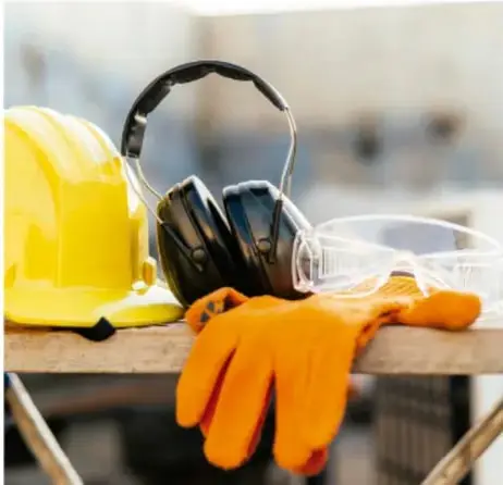 Foto de equipo de protección: casco amarillo, careta facial, auriculares de protección y guantes naranjas sobre una mesa.