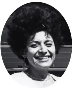 Fotografía en blanco y negro de Alejandra Jáidar Matalobos, mujer sonriente con cabello rizado.