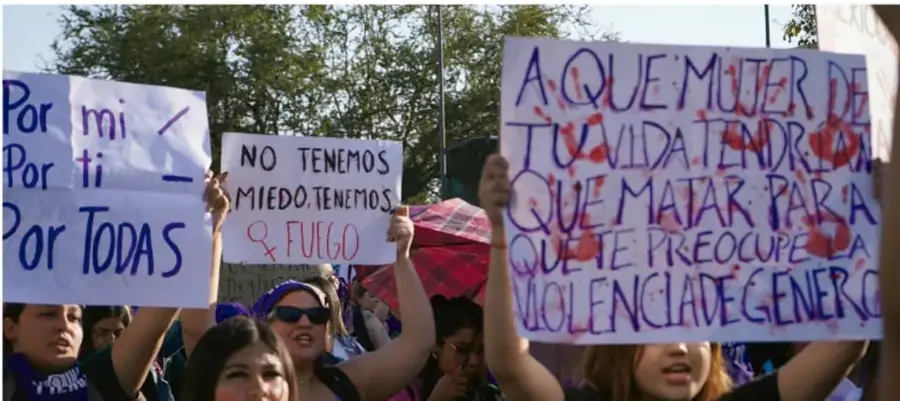 Fotografía de una marcha feminista: mujeres jóvenes con carteles que dicen 'Por mí - Por ti - Por todas', 'NO TENEMOS MIEDO. TENEMOS FÚGEO (fuego)' y 'A qué mujer de tu vida tendría que matar para que te preocupe la violencia de género', con manos pintadas de rojo en los carteles.