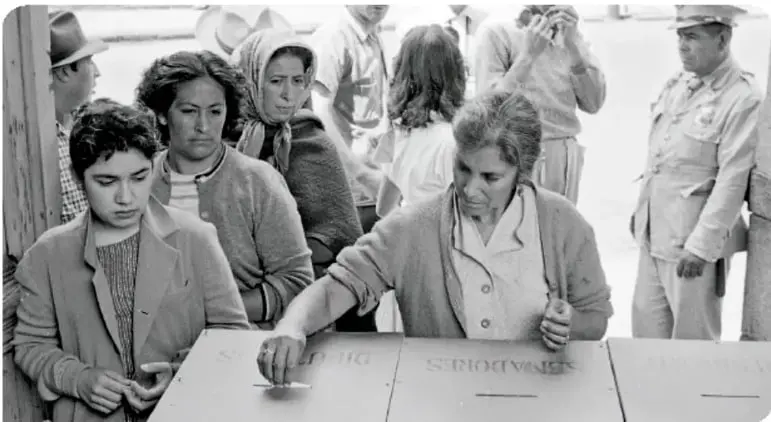 Fotografía en blanco y negro de mujeres votando en una casilla electoral.