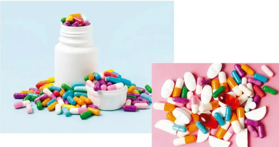 Frasco blanco de pastillas con cápsulas y tabletas de colores esparcidas sobre fondo azul claro.