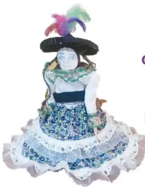 Fotografía de un muñeco con sombrero negro pequeño, plumas moradas, blusa blanca y enagua azul bordada con encaje.