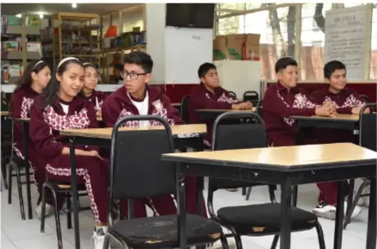 Fotografía de estudiantes de secundaria en uniforme bordado (color vino) sentados en pupitres de un aula, participando en clase.