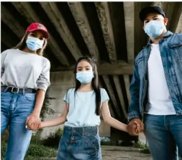 Familia (madre, hija y padre) usando cubrebocas y de pie bajo una estructura, ilustrando medidas de la vía respiratoria.