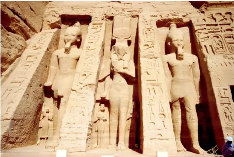 Fotografía de los colosos de Abu Simbel tallados en roca, con jeroglíficos y figuras de menor tamaño junto a las piernas de las estatuas.
