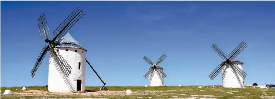 Tres molinos de viento blancos de estilo tradicional en un campo abierto bajo cielo azul, símbolo de aprovechamiento de la energía eólica.