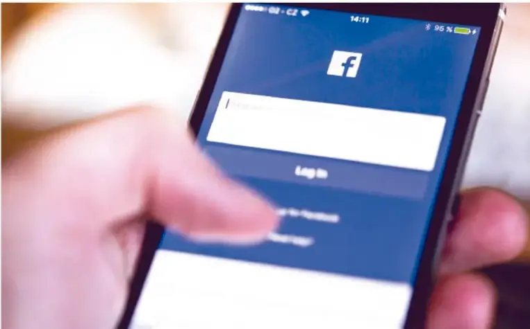 Fotografía de una persona sosteniendo un teléfono inteligente que muestra la pantalla de inicio de sesión de Facebook (campo de usuario y botón "Log In").