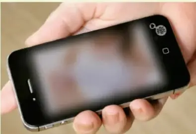 Mano sosteniendo un teléfono inteligente con la pantalla desenfocada, ilustrando el envío de mensajes (sexting).