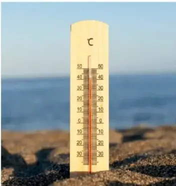 Termómetro clínico de vidrio sobre una roca junto al mar, con la escala en grados Celsius.