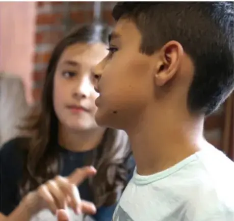 Fotografía de dos estudiantes, una niña y un niño, conversando y trabajando juntos, ilustrando la colaboración en un proyecto.