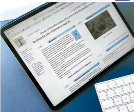 Tableta electrónica sobre escritorio mostrando una página tipo enciclopedia con un artículo ilustrado.