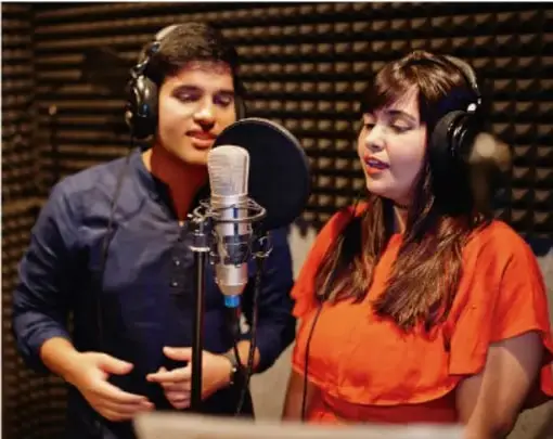 Fotografía de dos jóvenes con auriculares hablando frente a un micrófono de estudio, ilustrando la grabación de un podcast o programa de radio escolar.