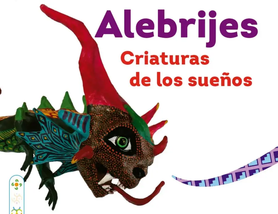 Fotografía de un alebrije escultural: criatura con cabeza de dragón (parda con punteado rojo, ojos verdes, cuernos rojos y verdes, lengua roja), alas azules decoradas con rombos y rayas, y lomo verde con espinas rojas. Al lado hay una cinta morada con grecas. Debajo del título 'Alebrijes' aparece el subtítulo 'Criaturas de los sueños' en rojo.