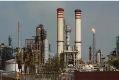 Fotografía de una refinería o planta industrial con chimeneas y torres de destilación, relacionada con la extracción y procesamiento de petróleo y gas.