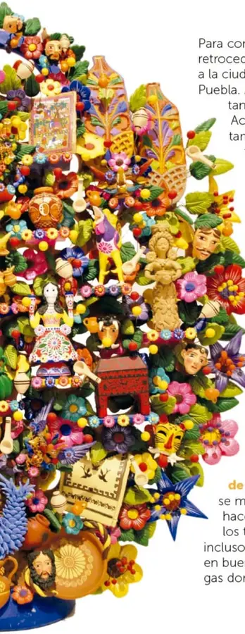 Árbol de la vida de barro con figuras religiosas al pie, frutas, flores rojas y moradas, aves, caritas pintadas y adornos muy coloridos.