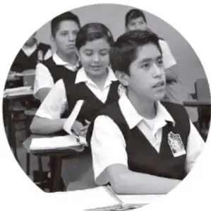 Fotografía en blanco y negro de un grupo de estudiantes de primaria en un salón de clases, uno de ellos escribiendo en su cuaderno.