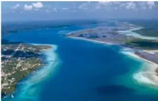 Vista aérea de una costa con aguas turquesa, arena blanca y una carretera junto al mar.