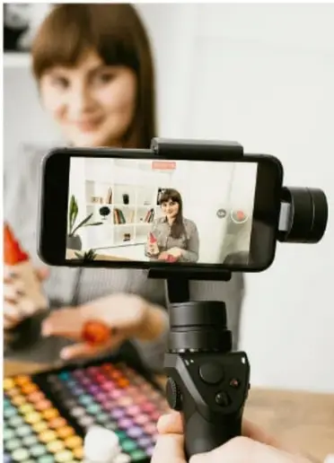 Persona grabando con un teléfono montado en un gimbal, frente a una paleta de maquillaje de colores, ilustrando la producción audiovisual.