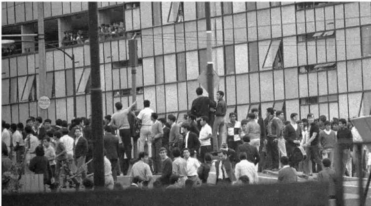 Fotografía en blanco y negro de un grupo numeroso de estudiantes reunidos frente a un edificio de varios pisos con ventanales, durante el movimiento estudiantil de 1968.