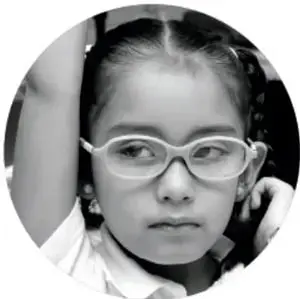 Fotografía en blanco y negro de una niña con lentes mirando a la cámara.