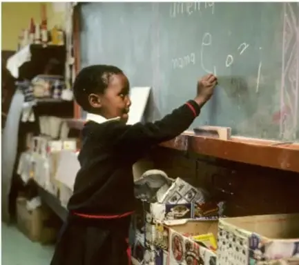Niño escribiendo en un pizarrón en un aula escolar, representando la ampliación de la educación.